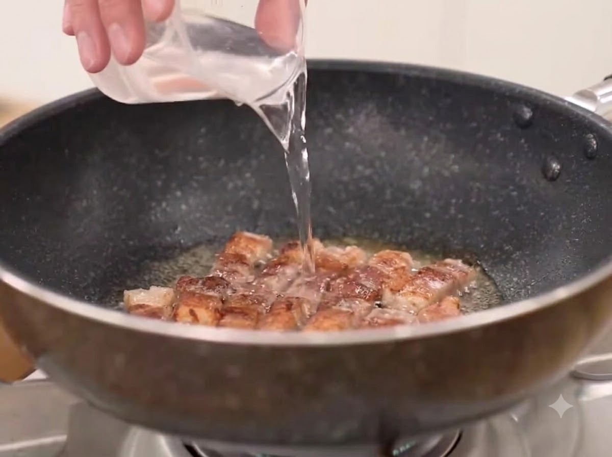 炒めた豚バラ肉が入ったフライパンに、水、粗挽き粉唐辛子、キムチを加えている様子