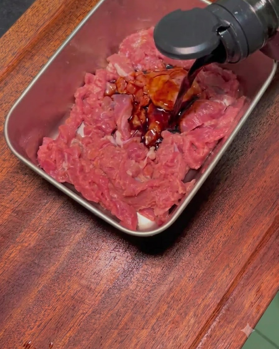 スライスした生の牛肉に黒いマリネ液をかけている様子。