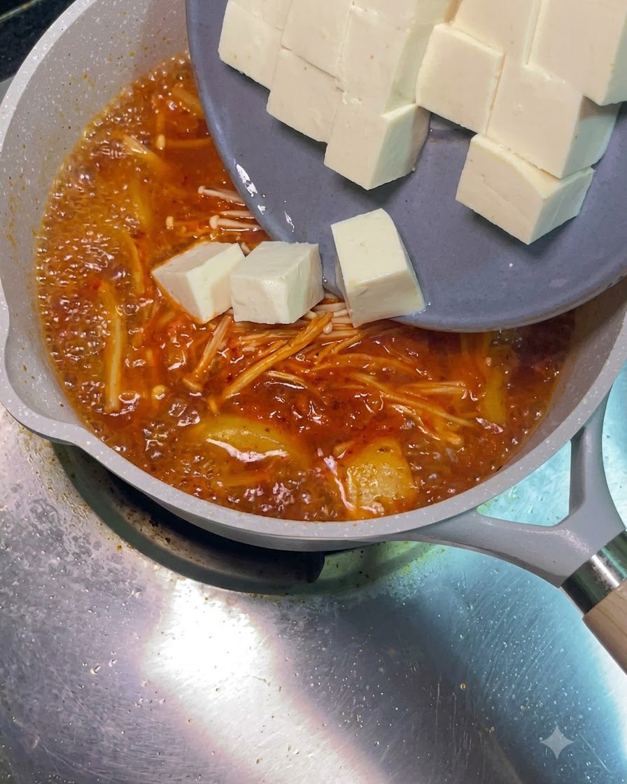 グレーのお皿から、サイコロ状に切った白い豆腐がぐつぐつ煮え立つ赤いスープに滑り落ちる様子。