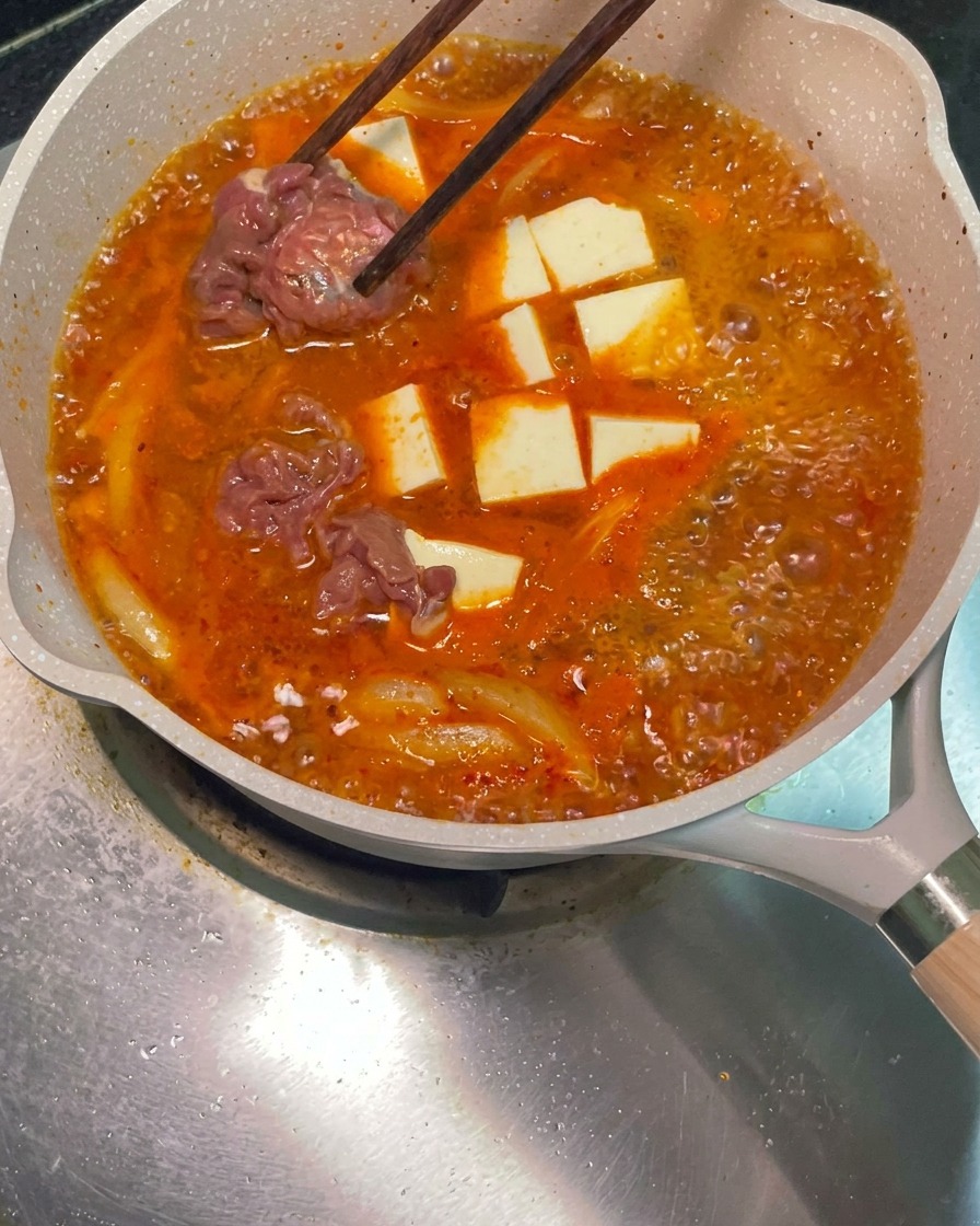 お箸を使って、下味をつけた生の牛肉をぐつぐつ煮え立つ赤いスープに入れている様子。