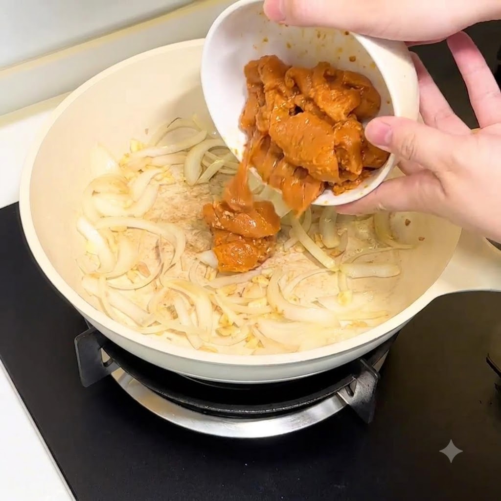 白いボウルから、玉ねぎとにんにくの入ったフライパンへ鶏むね肉のピースを入れている様子。