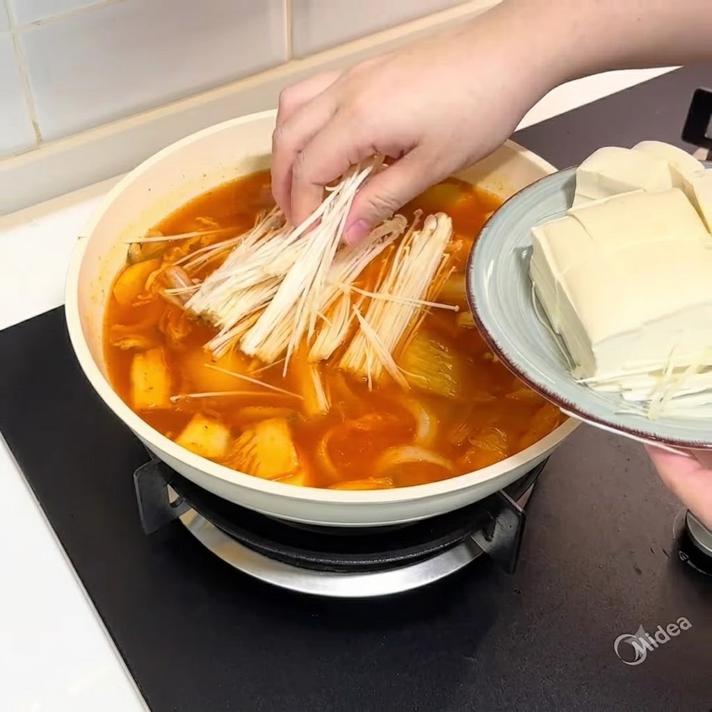 スープの入った鍋にエノキタケとスライスした豆腐を入れている様子。