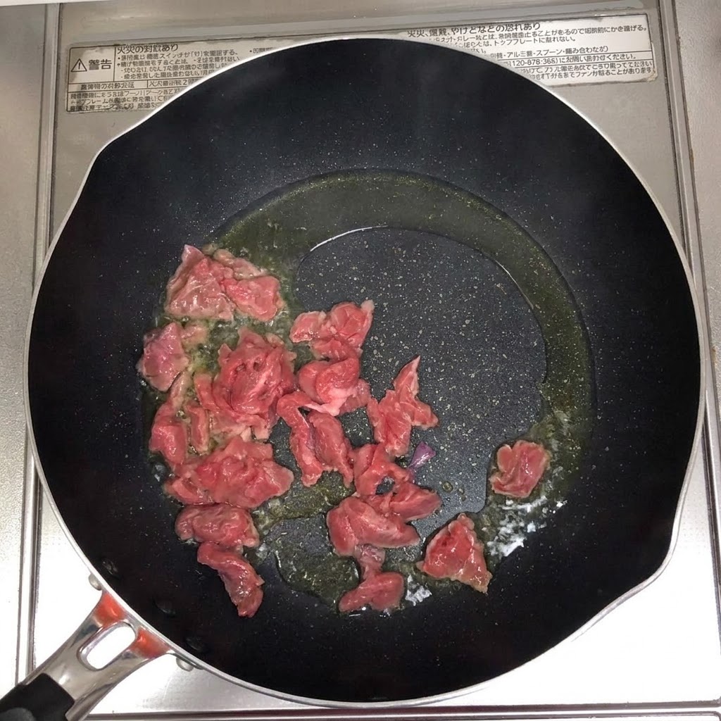 熱した油をひいたフライパンで、牛肉のスライスがジュージューと音を立ててきつね色に炒められている様子