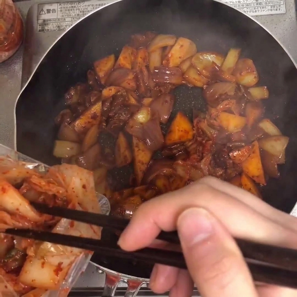 キムチがフライパンに加えられ、他の材料と一緒に混ぜ合わせられている様子