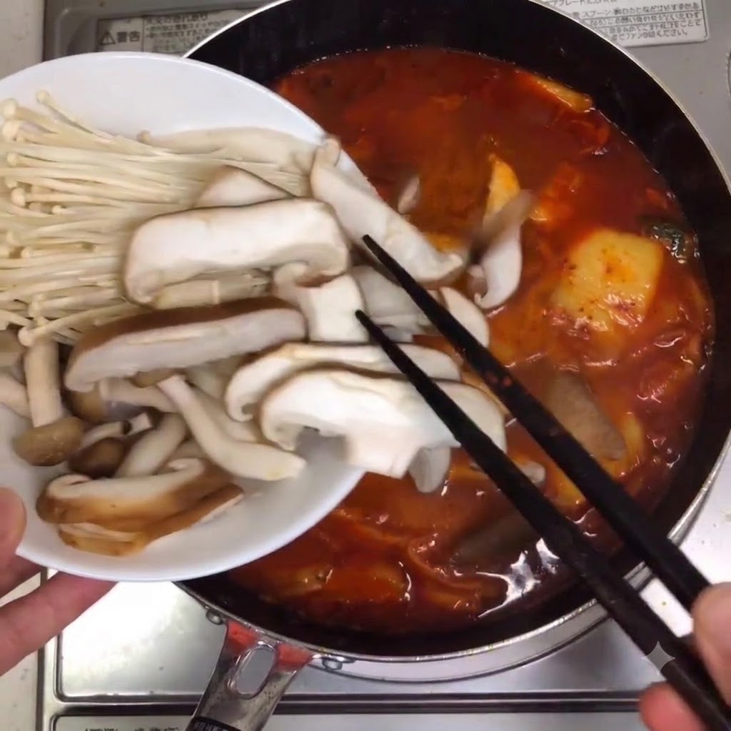 箸を使って、色々なキノコやエノキタケが煮立っているスープ鍋に入れられている様子