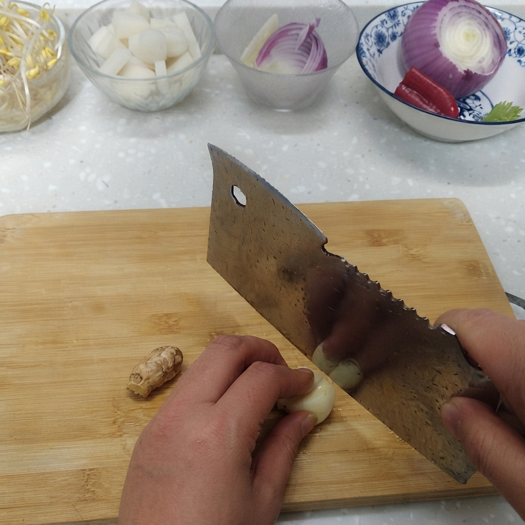まな板の上でスライスされているにんにくと新鮮な生姜の根、その隣にある材料のボウル。