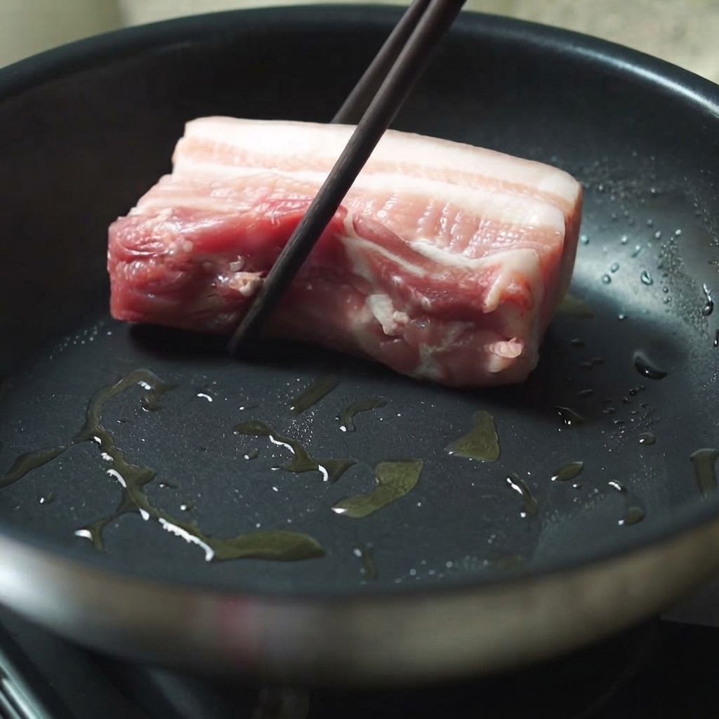菜箸を使って、油をひいた熱々のフライパンに厚切りの豚バラ肉を入れている様子。