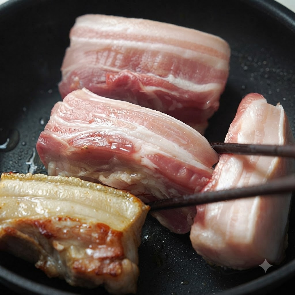 フライパンの中で菜箸で裏返される複数の豚バラ肉。1つのピースにはこんがりとした焼き色がついている。