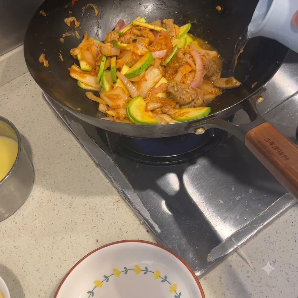 具材の入った中華鍋に、明るい色のケトルからお湯が注がれているところ。