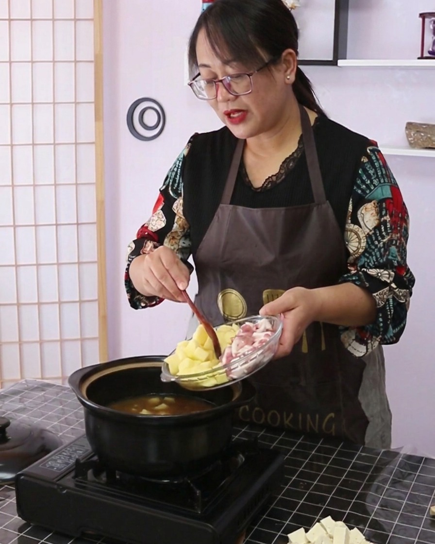 ガラス皿から、サイコロ状のじゃがいもとスライスした豚バラ肉を調理鍋に入れている様子。