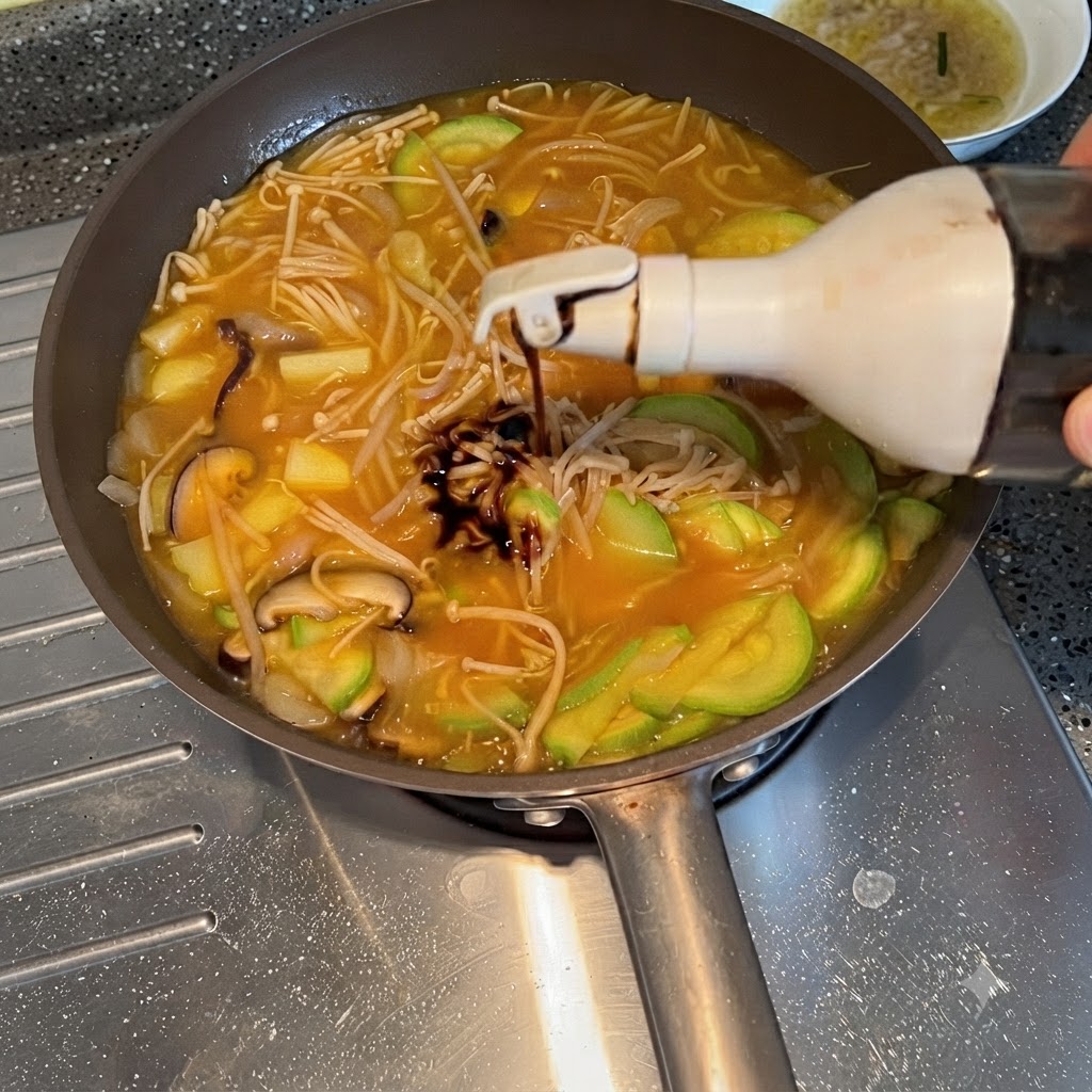 煮込んでいる野菜のスープに醤油がボトルから絞り出されている様子。