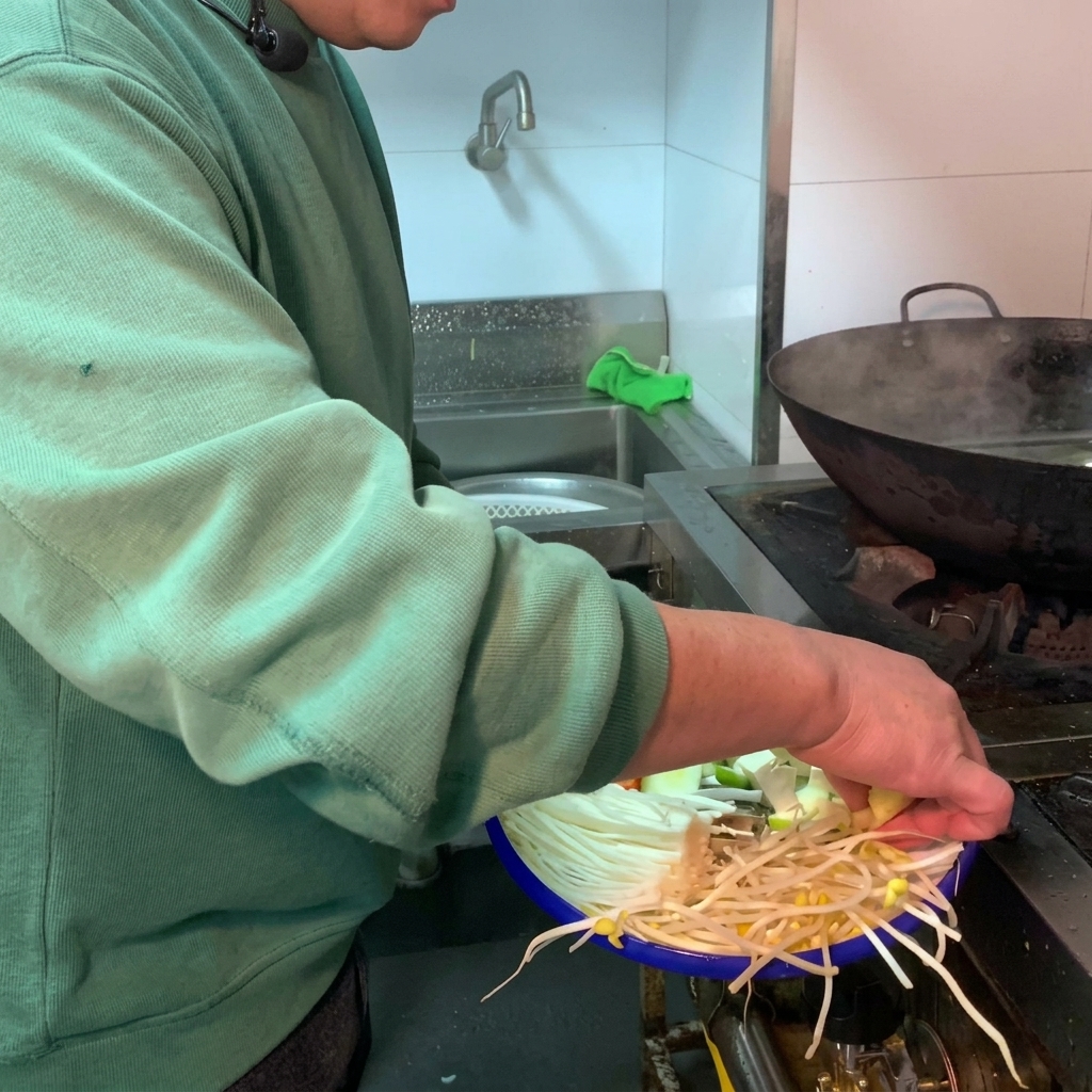 水を入れた黒い土鍋に、新鮮な野菜と白い豆腐を入れている様子。