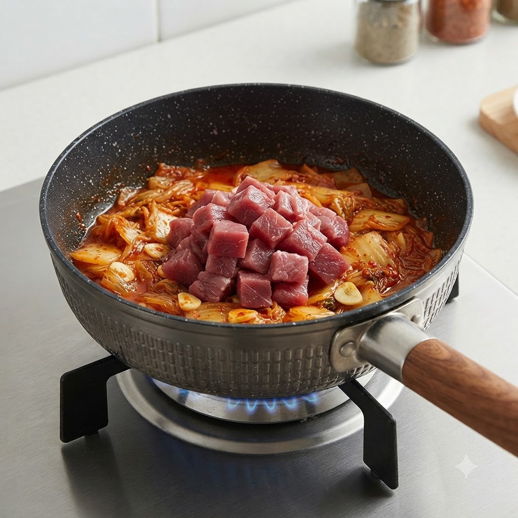 鍋の中で炒めたキムチの上に生の角切り牛肉をのせている様子