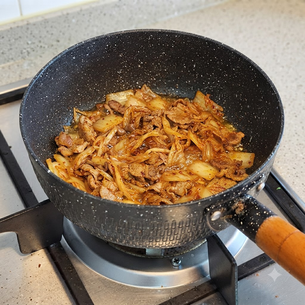 炒めたキムチと牛肉が入った鍋に水を注いでいる様子