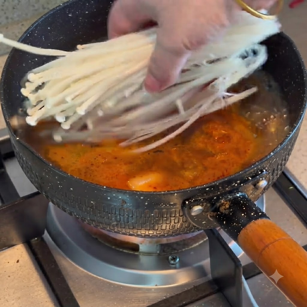 キムチと牛肉の煮立ったスープが入った鍋に、えのきだけを加えている様子