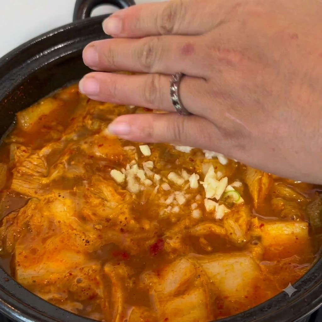 みじん切りにしたにんにくを、グツグツと煮立つスープの鍋に手でパラパラと振り入れている様子。