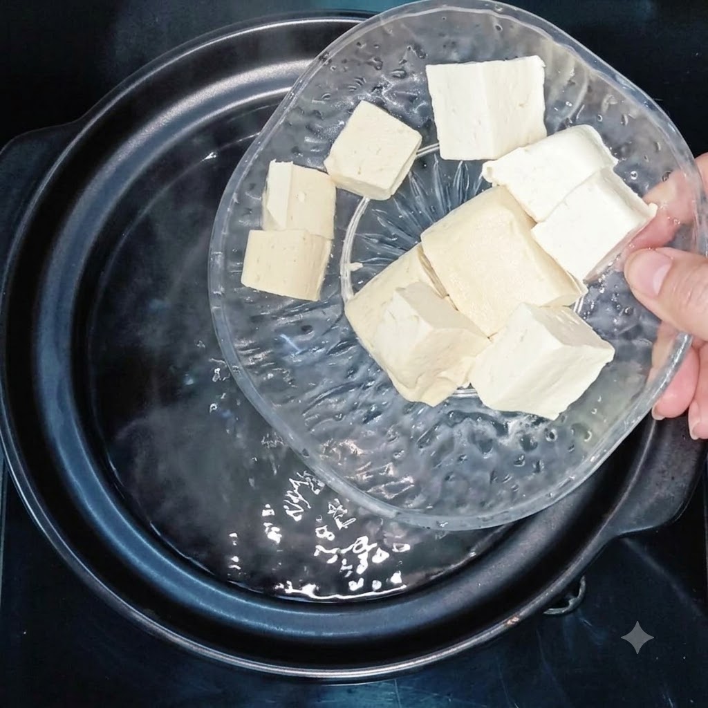 透明なガラス皿から、沸騰したお湯の入った鍋に豆腐のキューブを入れているところ。