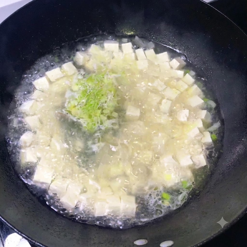 豆腐と刻んだネギが入ったグツグツと煮える鍋に、調味料を振りかけている様子