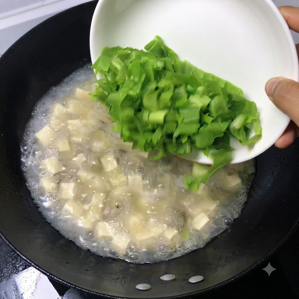 白いお皿から新鮮な刻み青菜の葉を、煮立っているスープの鍋に滑り込ませている様子