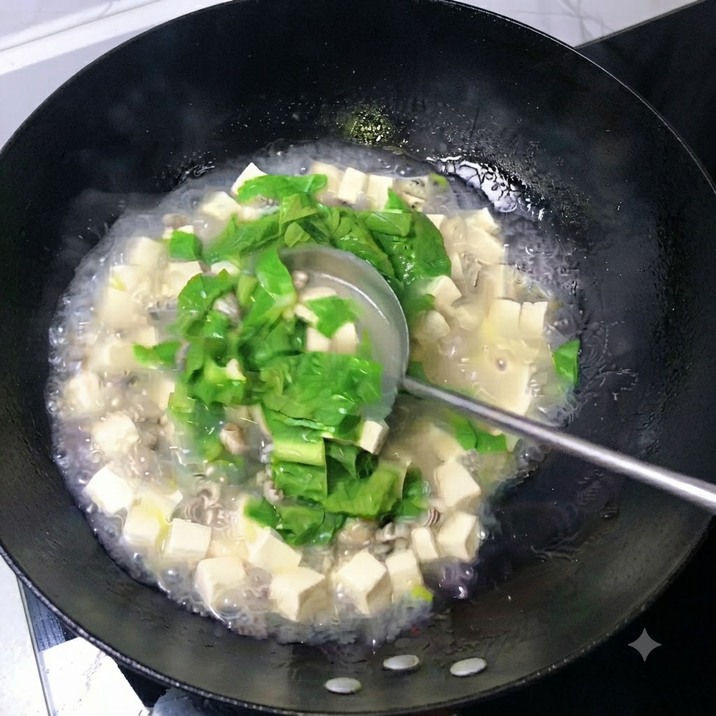 中華鍋の中で、豆腐の角切り、牡蠣、青葉が入った乳白色のスープをおたまですくい混ぜている様子