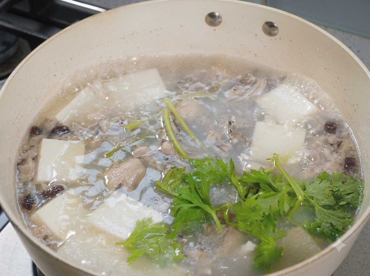 牡蠣と豆腐のスープがぐつぐつと煮える鍋の上に、新鮮なセロリの葉が散らされている様子。