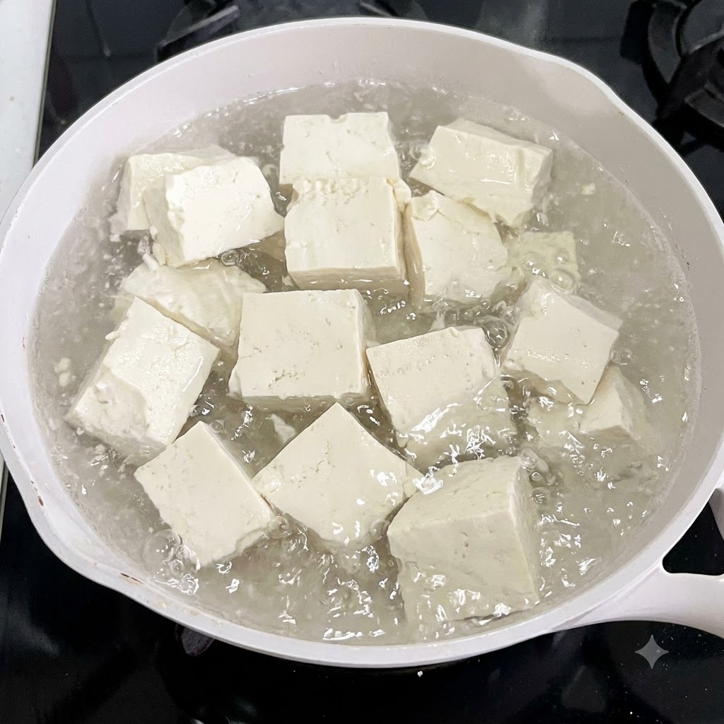 生姜のスライスと一緒に白いお湯の鍋で茹でられている豆腐のキューブ