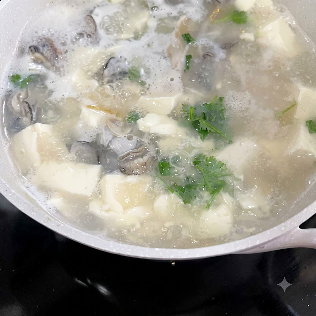グツグツと煮える牡蠣と豆腐のスープに刻んだパクチーと青ネギが加えられている様子