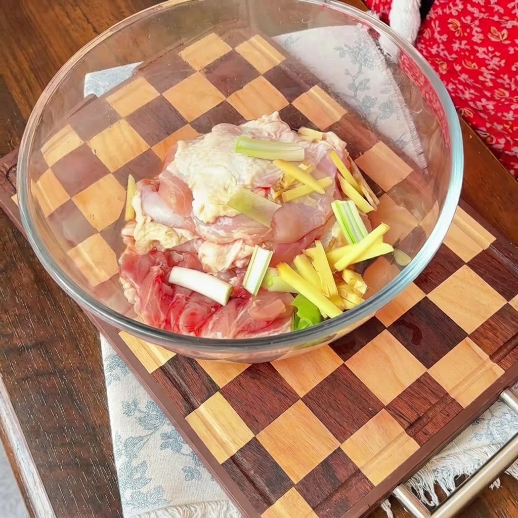 ガラスボウルに入った生の鶏肉の上に、スライスした赤玉ねぎ、万能ねぎ、千切り生姜が乗せられているところ。