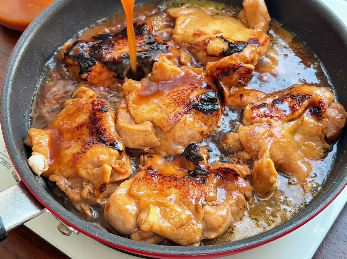 こんがり焼けた鶏肉が入ったフライパンの上から、濃い茶色のタレが高所から注がれているところ。