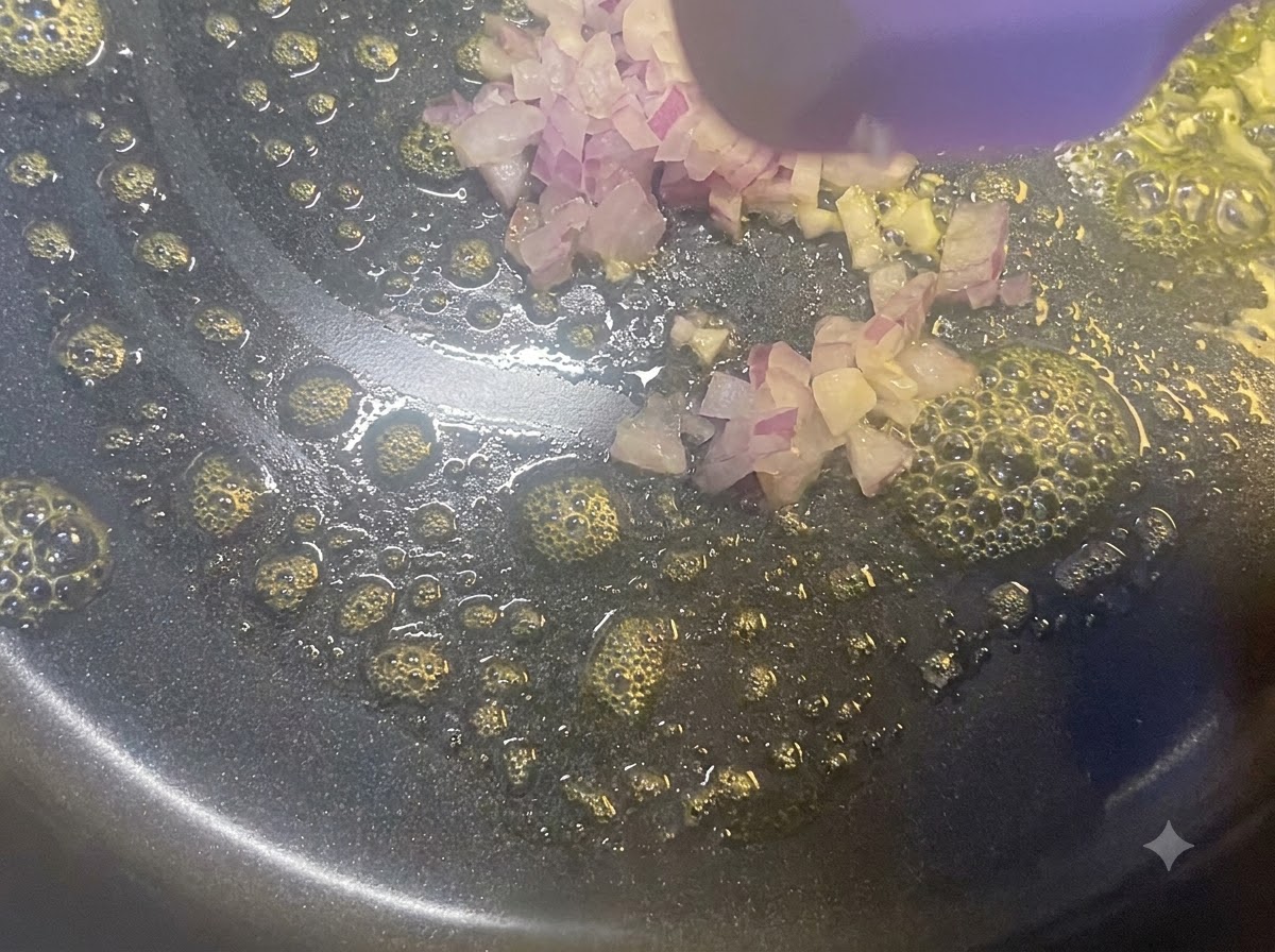 木製のヘラを使い、バターを溶かしたフライパンでみじん切り玉ねぎを炒めている様子。