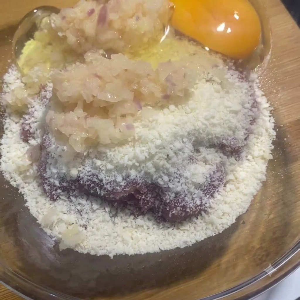 肉と玉ねぎの入ったガラスボウルの中に生の卵黄と卵白が入っている様子。