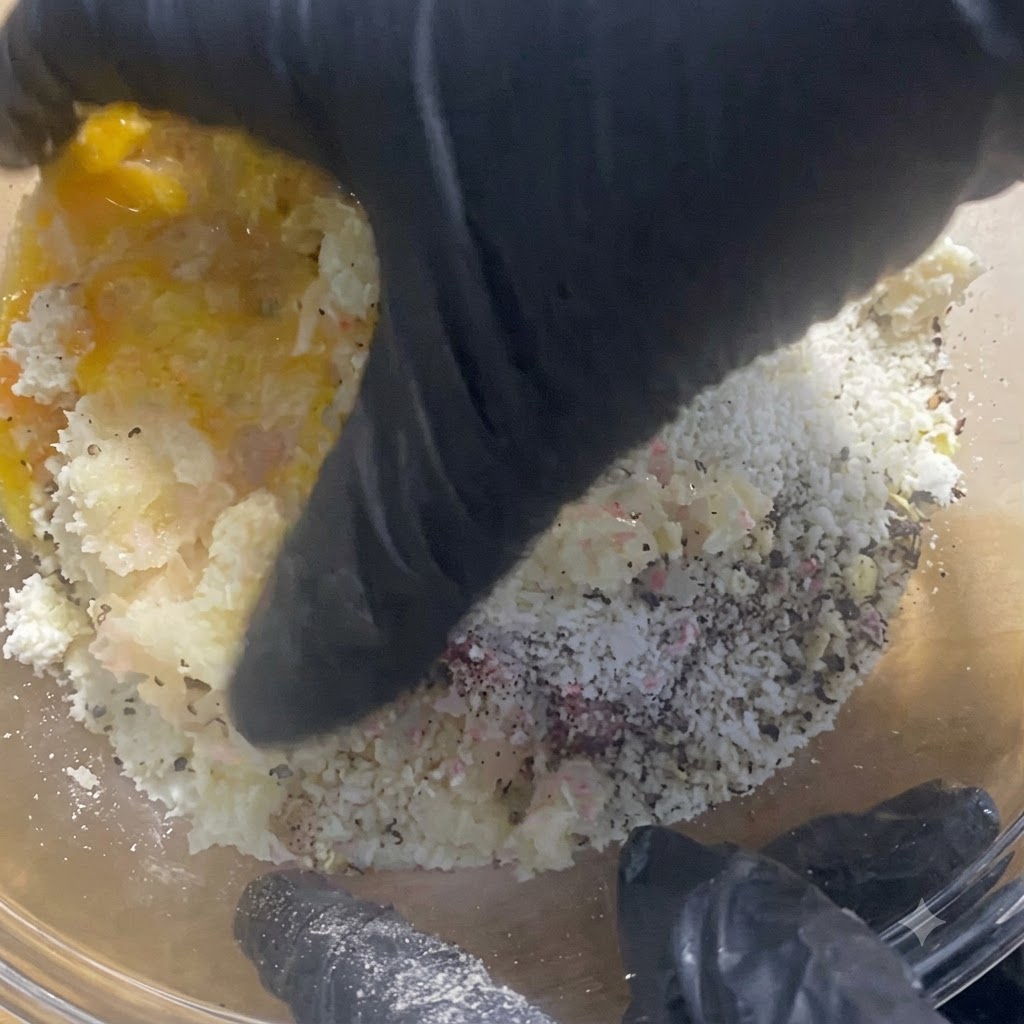 手袋を着用した手がガラスボウルの中で肉の具材をしっかりと混ぜ合わせ、こねている様子。