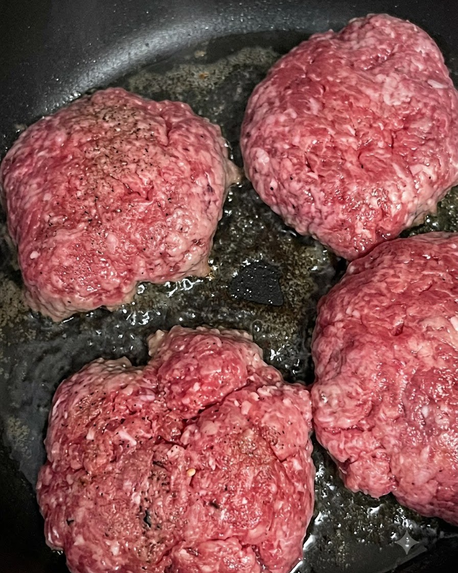 熱したフライパンの中でジューシーに音を立てて焼き色がつく4枚の生のビーフパティ。
