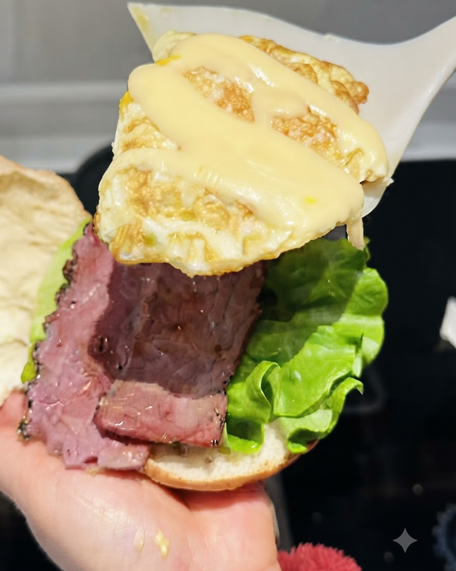 チーズを溶かした目玉焼きを、ヘラですくってバーガーの具材の上に重ねようとしている様子。