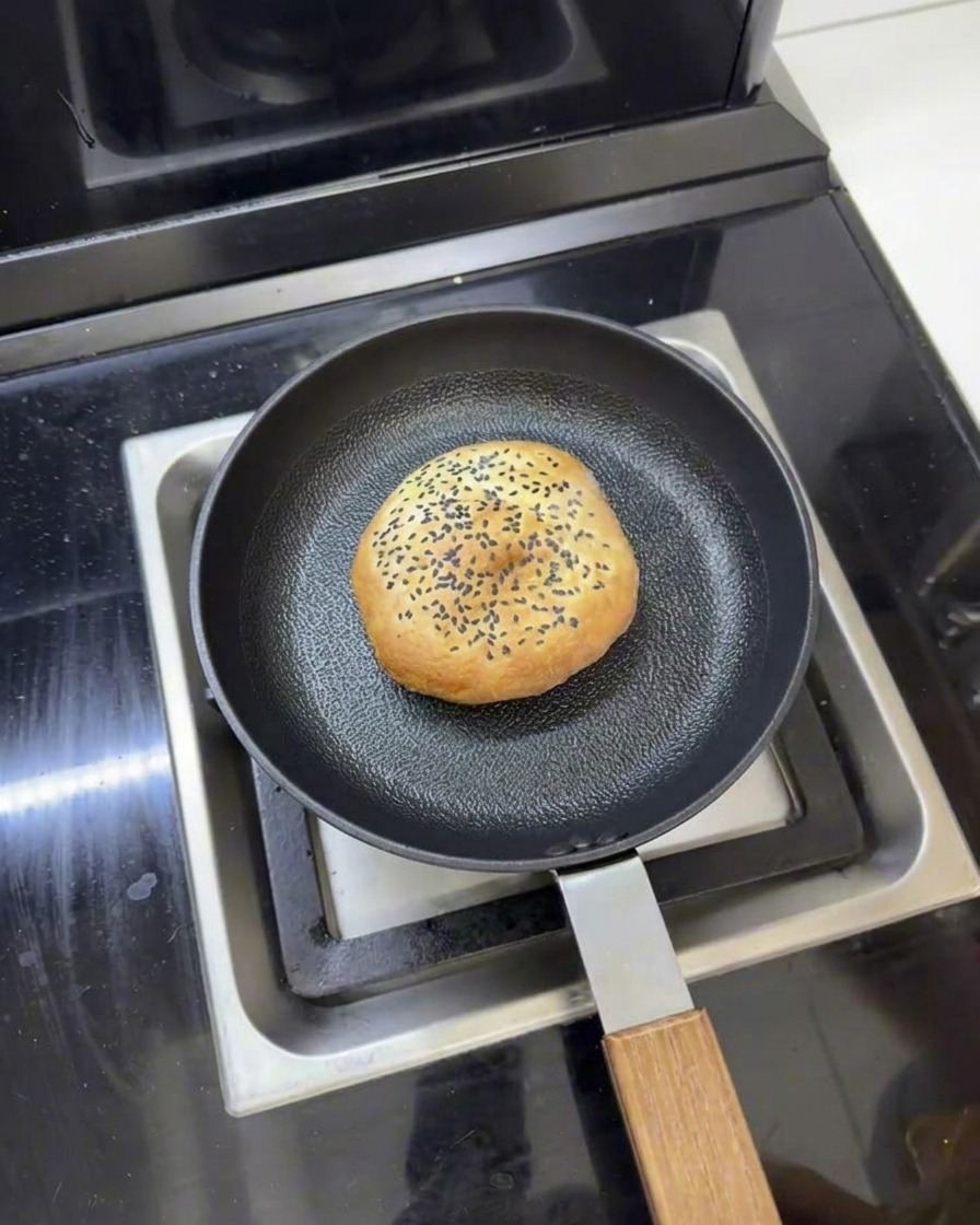 フライパンの中に置かれ、周囲に水があり、蓋をして蒸し焼きにする準備ができているバターバーガーバンズ。