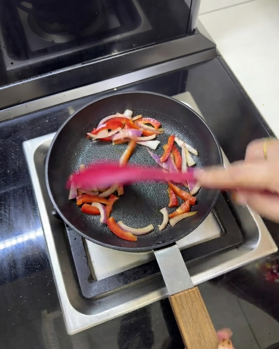 フライパンの中で赤玉ねぎやパプリカと一緒に炒められている、調理済みの肉の細切り。