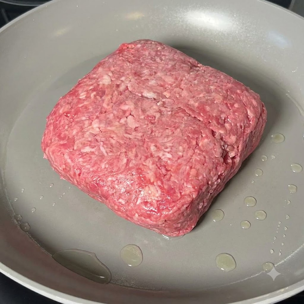 広いフライパンの中で、木製のヘラを使って牛ひき肉のかたまりをほぐしながら炒めている様子。
