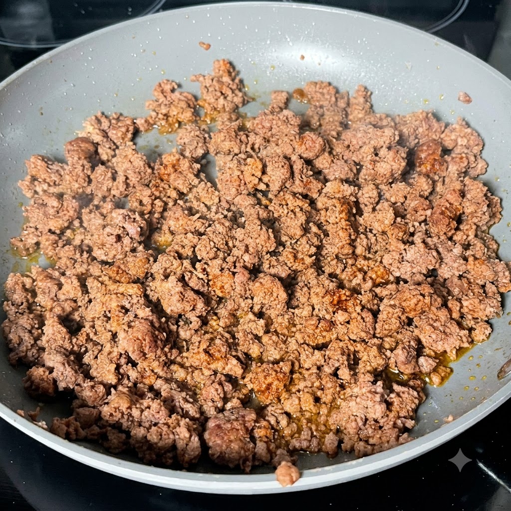 フライパンで炒めたひき肉の上に、色の濃いウスターソースがかけられている様子。