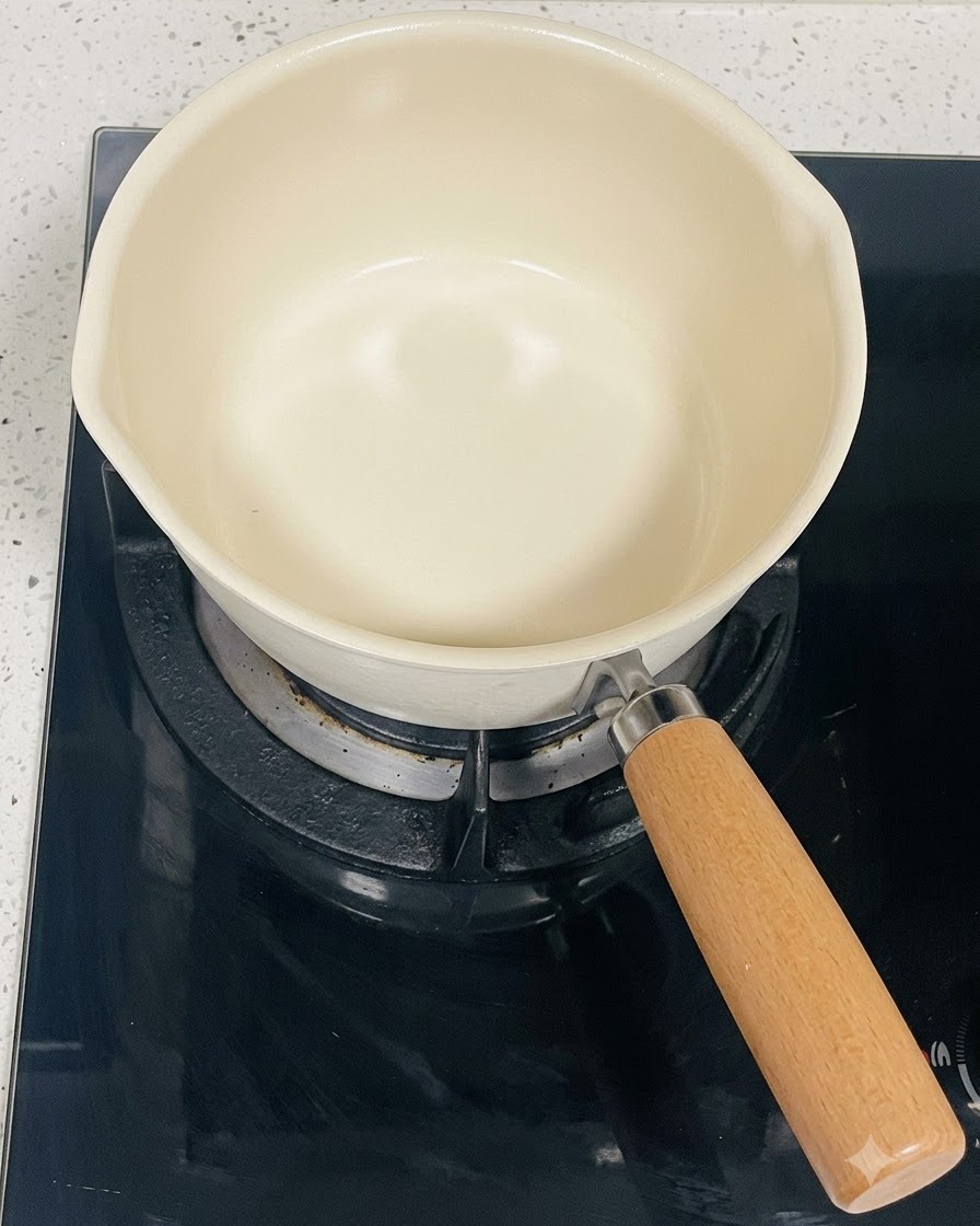 黒いIHクッキングヒーターの上に置かれた、クリーム色のきれいな片手鍋。