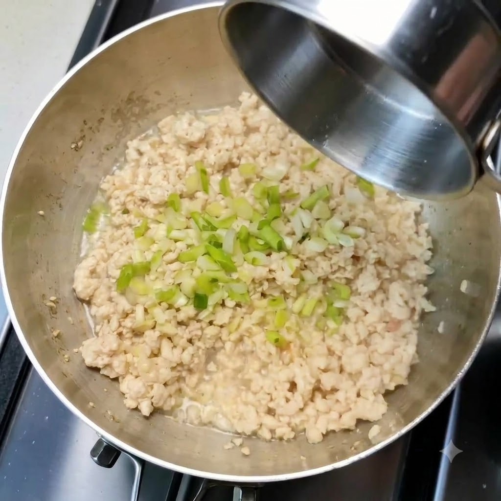 炒めた鶏ひき肉が入ったフライパンの上に、刻んだ青ネギとにんにくが散りばめられている様子。