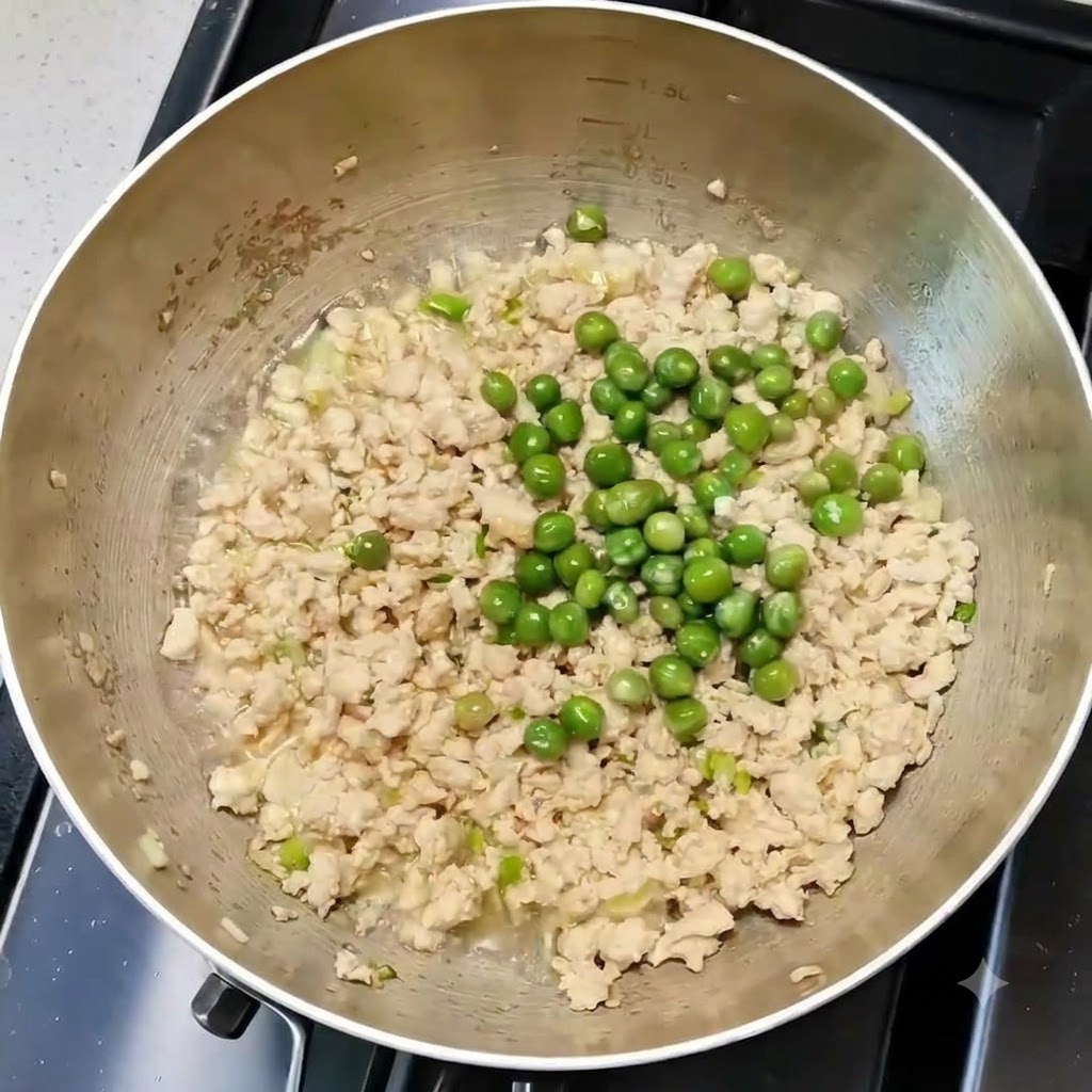 調理中のフライパンの中で、鶏肉や香味野菜とグリーンピースが均一に混ぜ合わされている様子。