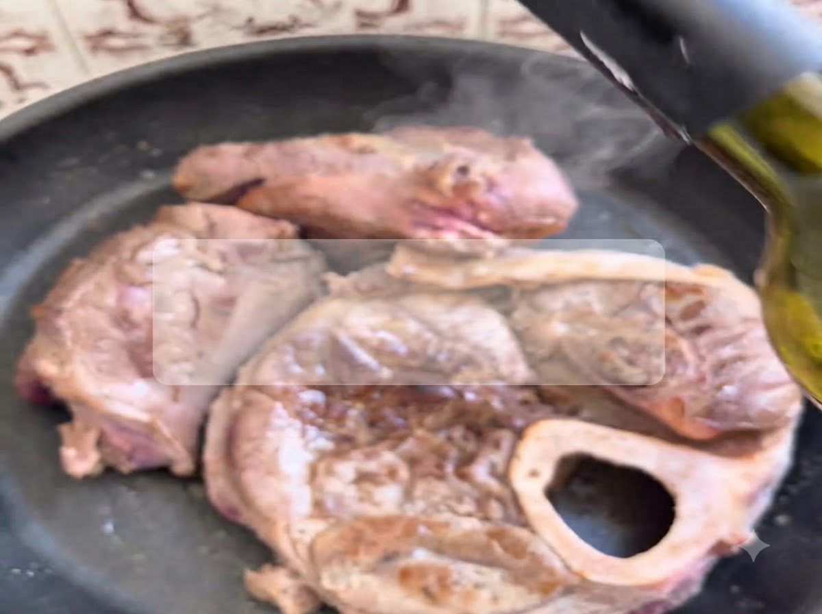 熱々のフライパンでジューシーに焼かれている牛肉の上に、ボトルから赤ワインが注がれている様子。