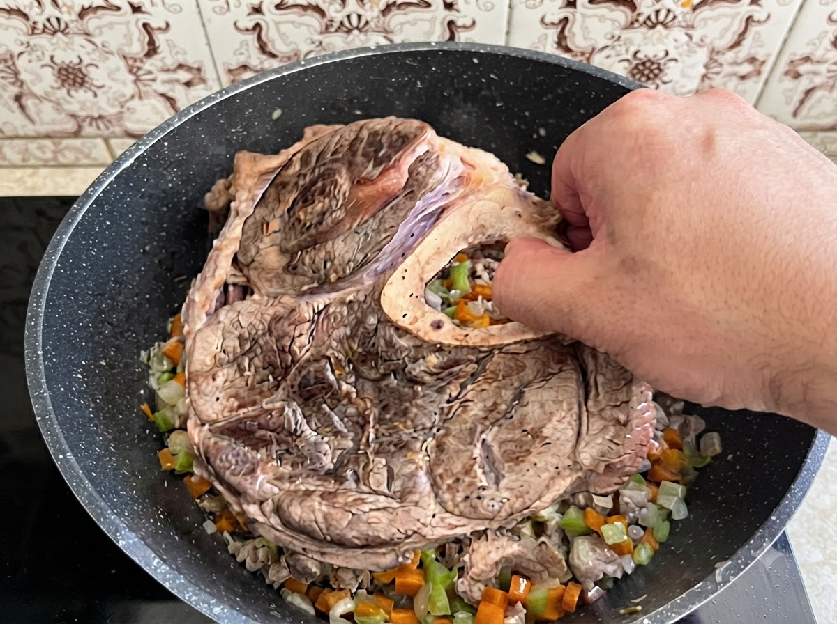炒めたみじん切り野菜の入った鍋に、大きな牛すね肉と骨を片手で慎重に入れている様子。