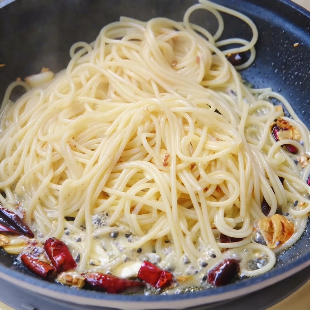 フライパンの中で、スパゲッティをコリアンダーの茎と茹で汁と一緒に和えている様子。