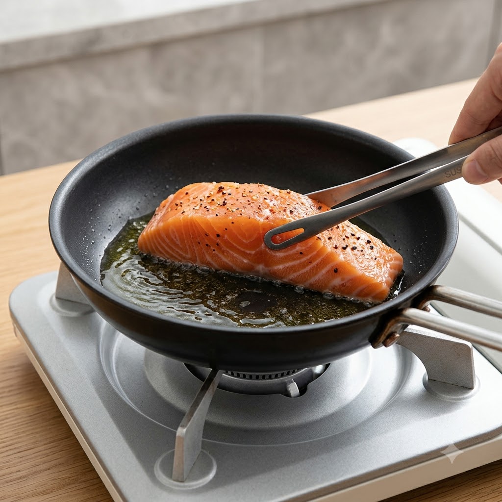 キッチントングを使い、下味をつけたサーモンフィレを皮目を下にして熱したフライパンに入れている様子。