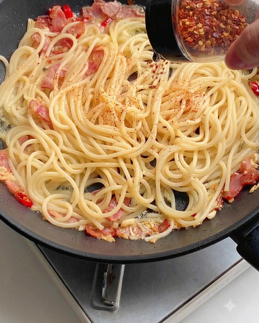 フライパンの中のスパゲッティの上に、赤色のチリパウダーが均等に振りかけられている様子。