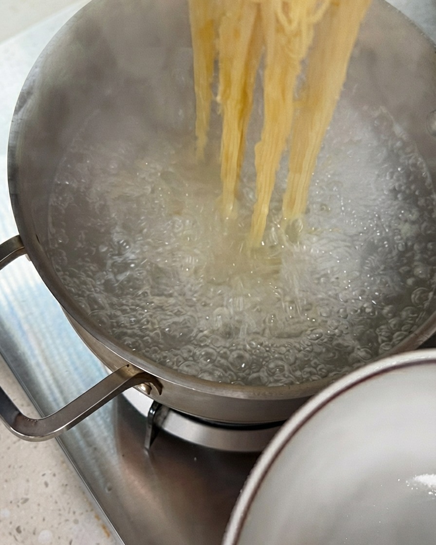 トングを使って、沸騰した鍋から茹で上がった麺を持ち上げている様子。