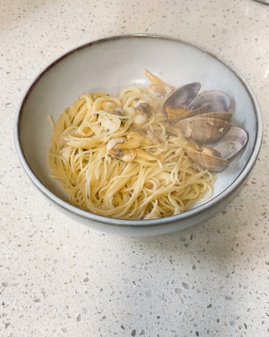 調理されたあさりと出汁が入ったフライパンに、冷たいバターの小片を落とし入れている様子。