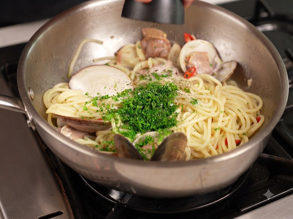 刻んだ緑色のパセリがトッピングされたパスタとアサリのフライパンの上で、ミルから黒こしょうが削りかけられている様子