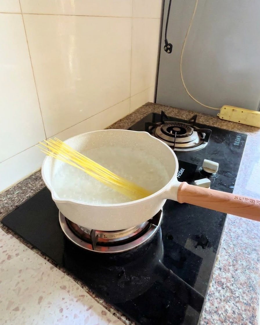 コンロの上の沸騰した鍋に、乾燥スパゲッティの麺を斜めに入れている様子